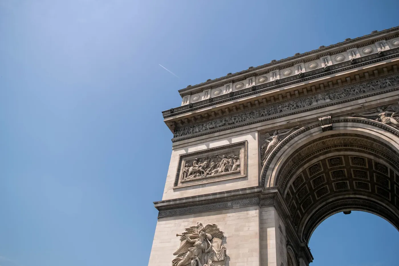 The Arc de Triomphe against a blue sky, carved friezes and the vault of the arch