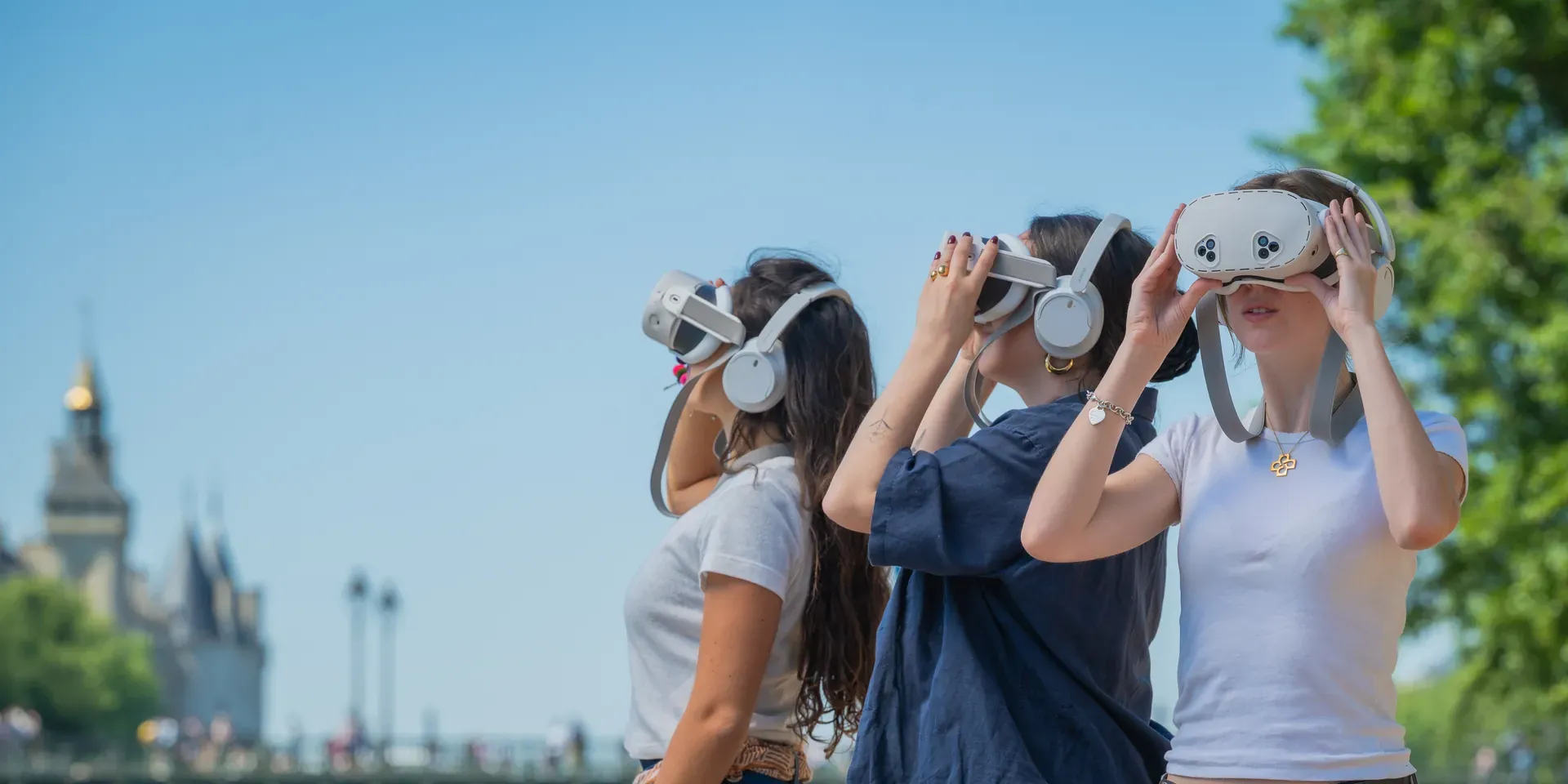 Trois visiteuses observent Paris aux Jumelles de réalité virtuelle Timescope, sur les quais de Seine face à la Conciergerie