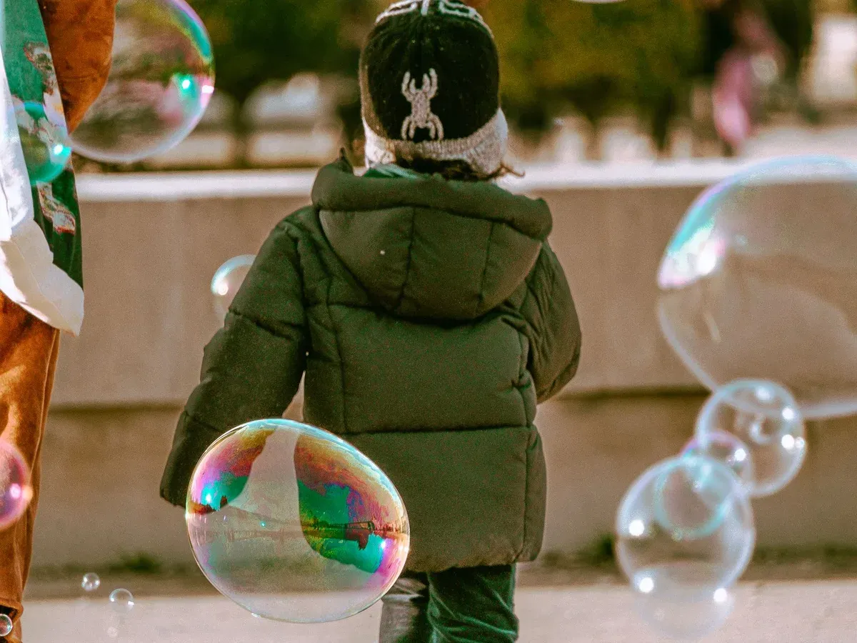 Enfant en doudoune courant après des bulles de savon géantes dans un jardin parisien en automne