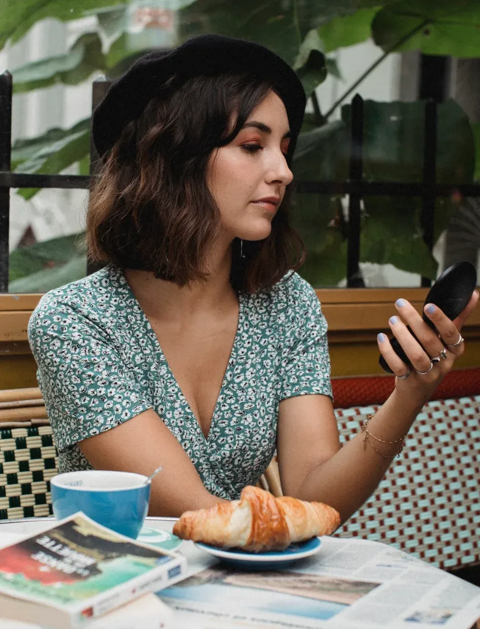 A woman in a black beret at a Parisian café terrace, croissant and coffee on the table