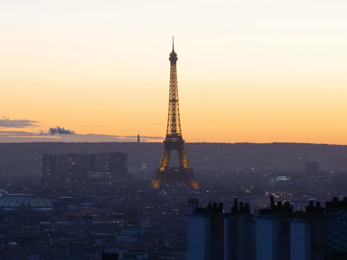 La Tour Eiffel se détache sur un ciel orange au-dessus des toits de Paris, vue depuis Montmartre à la tombée du soir