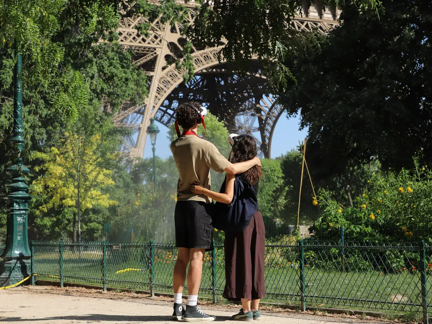 Un couple enlacé, casques Timescope sur la tête, regarde la Tour Eiffel depuis le Champ-de-Mars