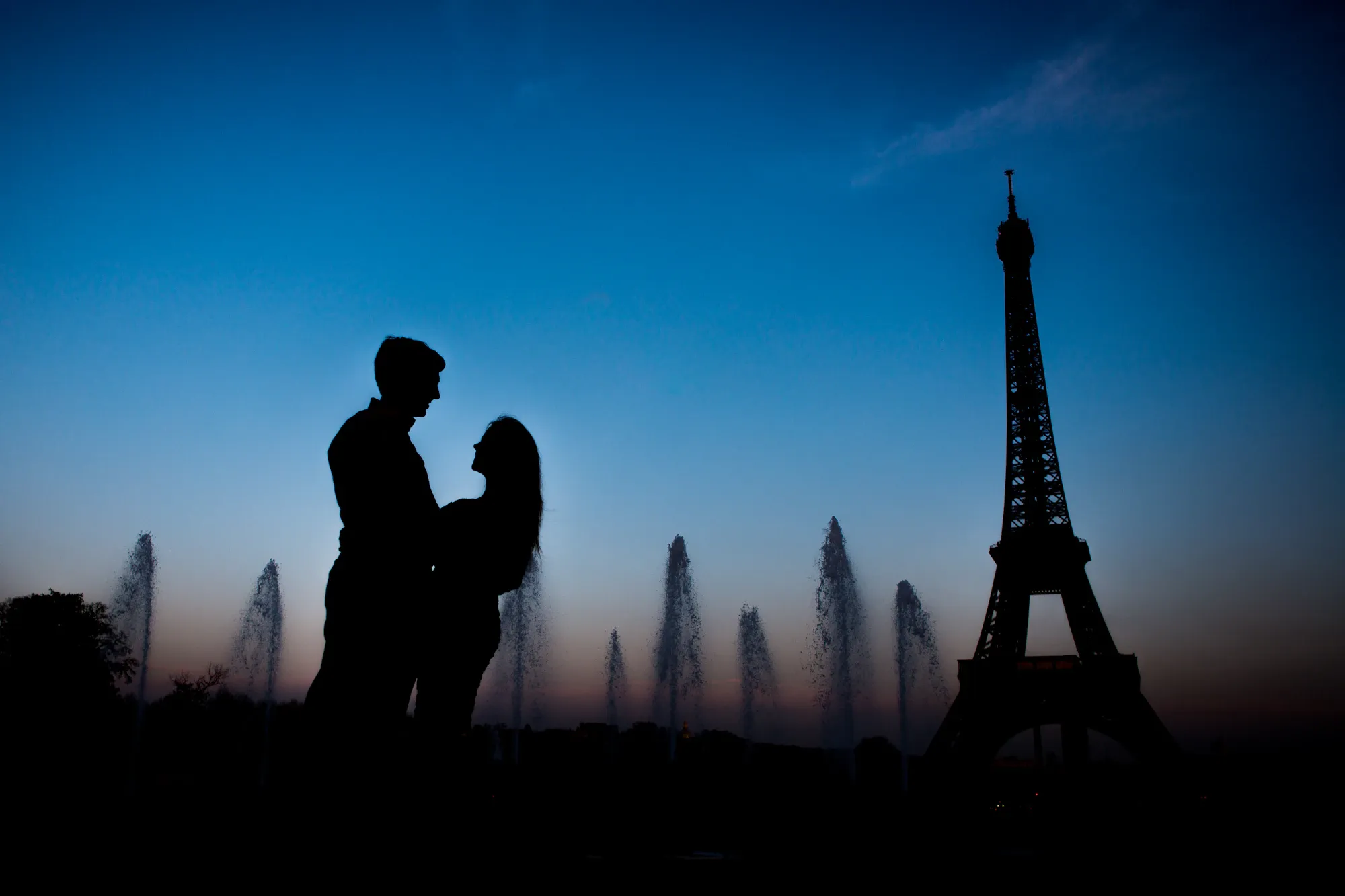 Silhouette of a couple facing the Eiffel Tower at dusk, in front of the Trocadéro fountains