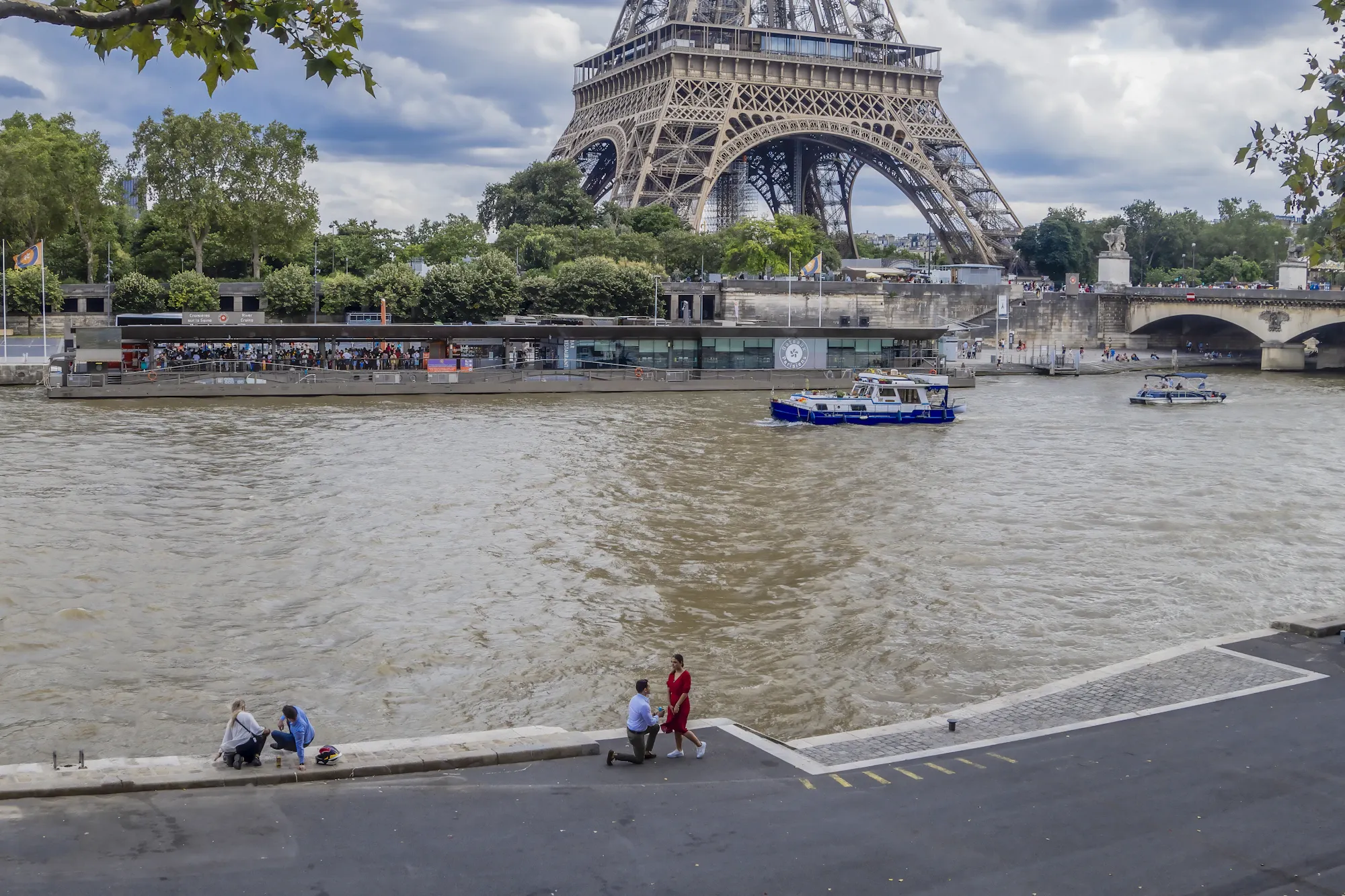 A man on one knee proposing on the banks of the Seine, the Eiffel Tower behind them