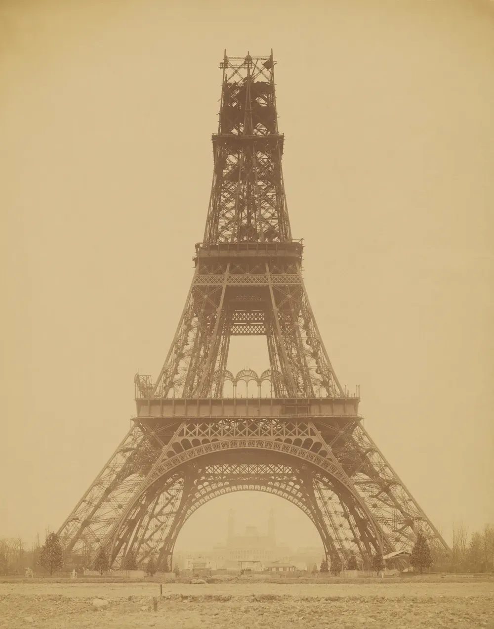 La Tour Eiffel en construction, le troisième étage encore inachevé, vue frontale depuis le Champ-de-Mars avec le palais du Trocadéro sous l'arche