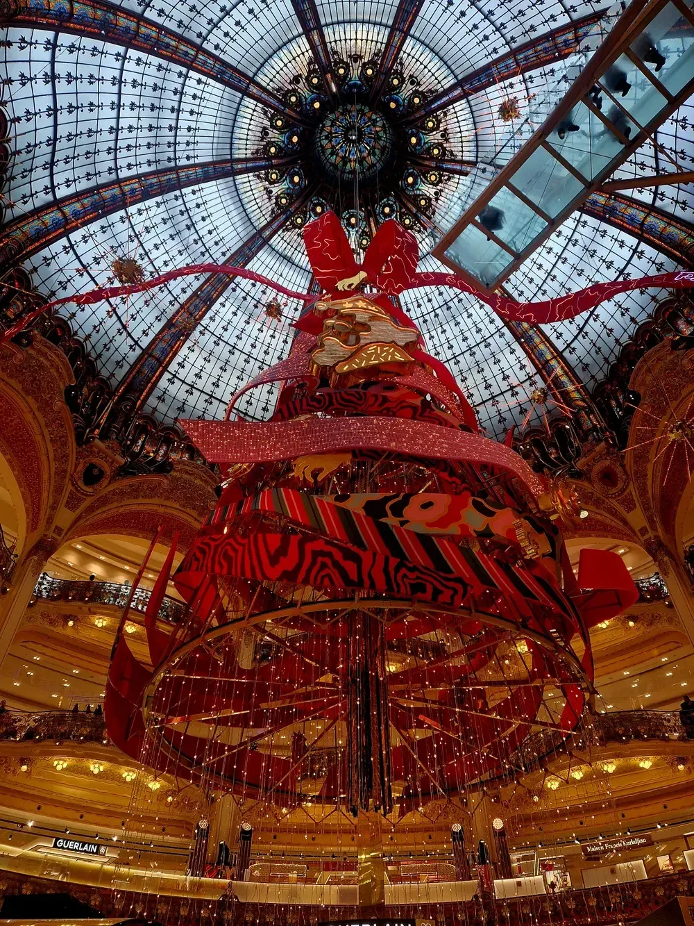 The giant Christmas tree under the stained-glass dome of the Galeries Lafayette Haussmann, decorated in red, with the balconies of the store around it