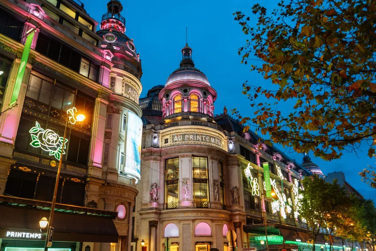 La façade du Printemps illuminée à la tombée du soir, sous les feuillages d'automne du boulevard Haussmann