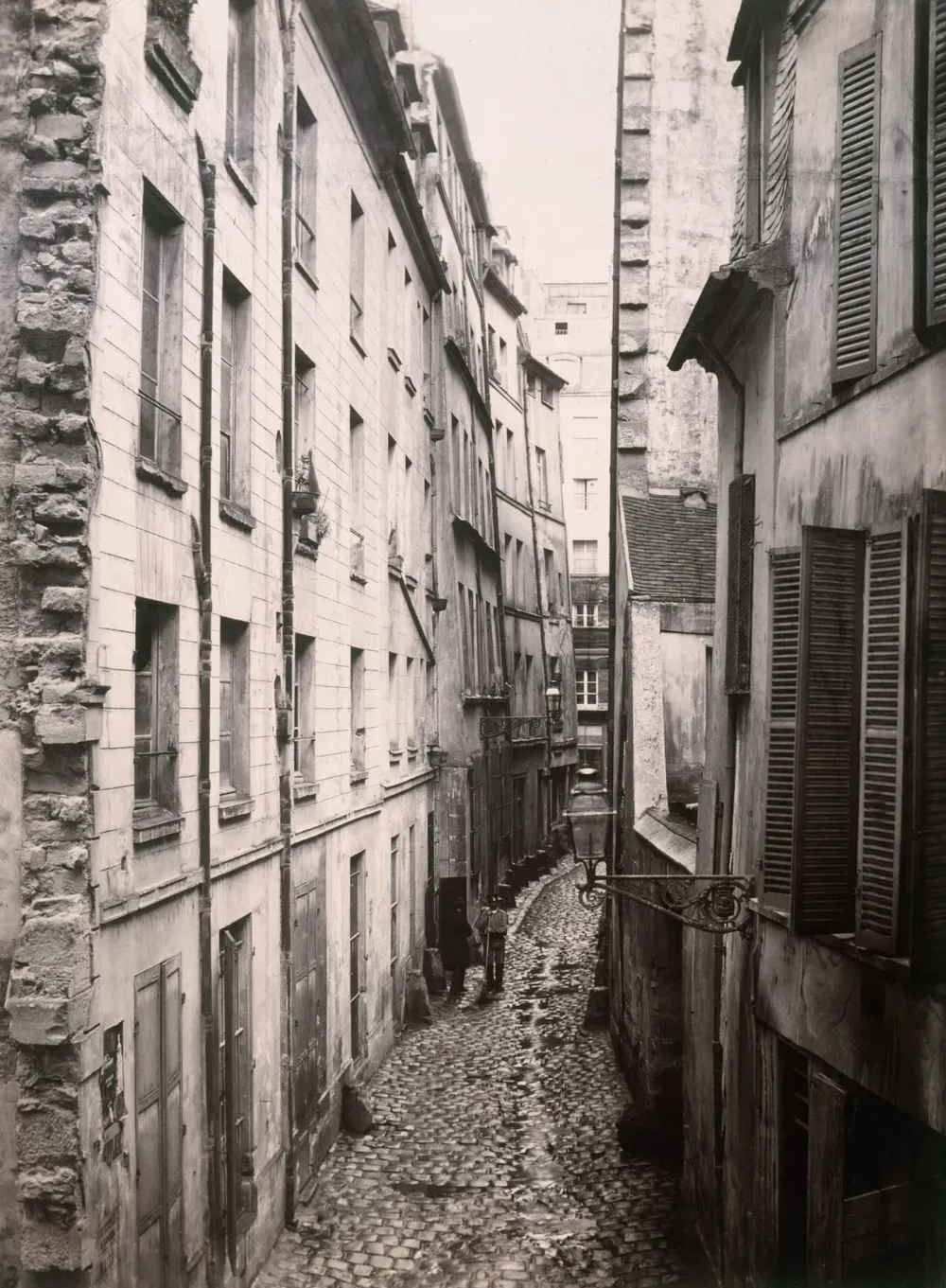 La rue Gervais-Laurent, ruelle étroite et pavée de l'île de la Cité, immeubles vétustes de part et d'autre, deux silhouettes immobiles au fond