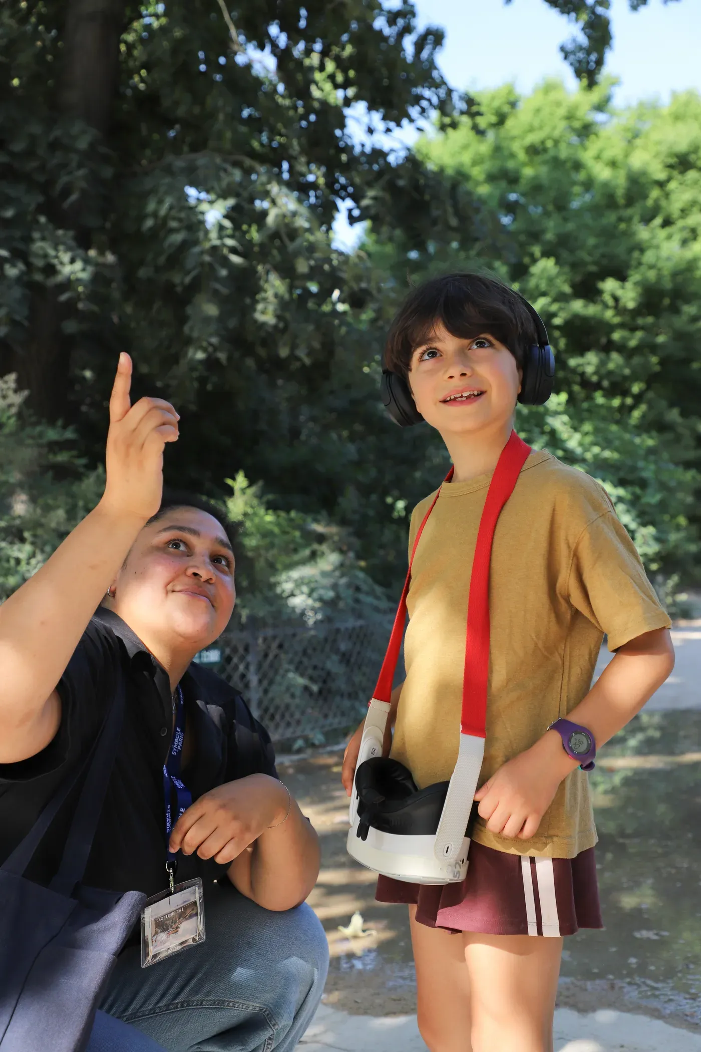 A Timescope guide, crouching, points to a spot in the sky for a child wearing headphones and binoculars