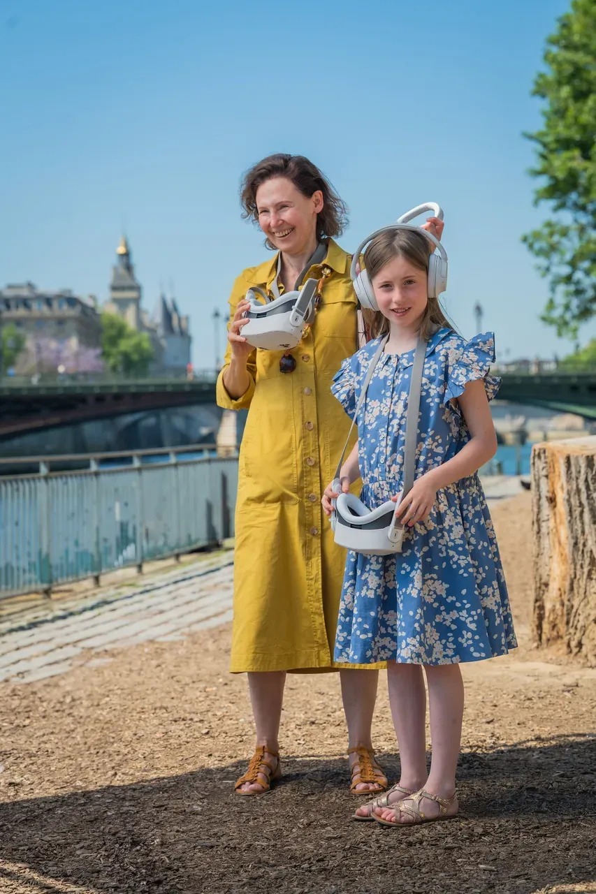 A mother and daughter discovering the virtual-reality binoculars on the banks of the Seine, the Conciergerie in the background