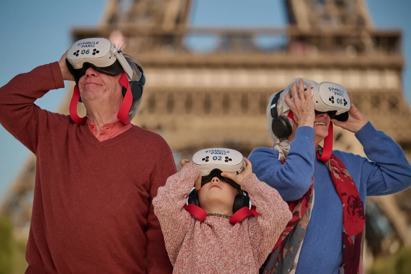 Three generations raise virtual-reality binoculars towards the Eiffel Tower, a child in the middle