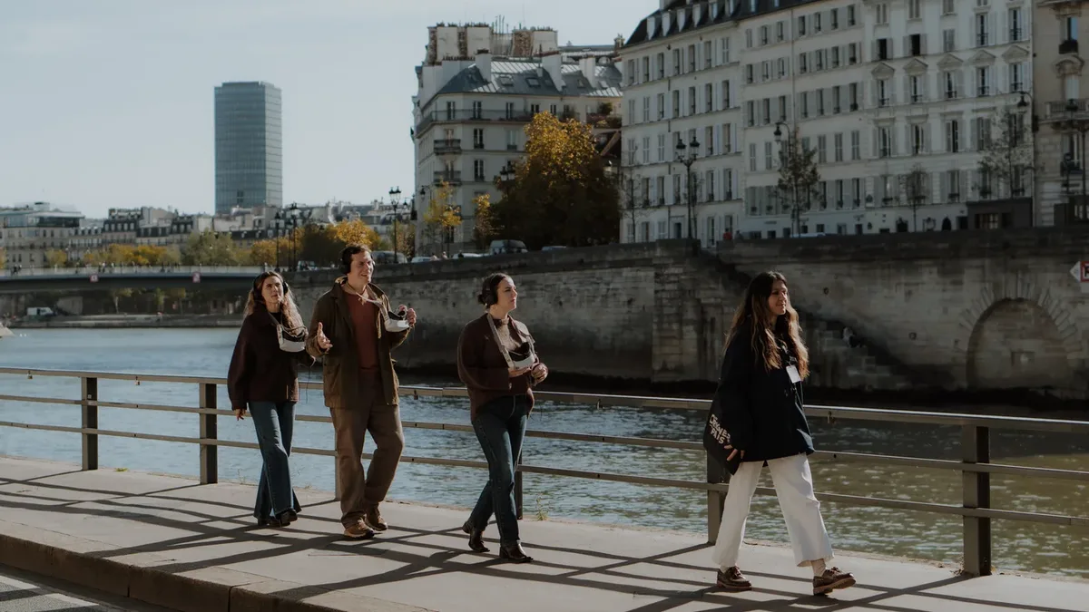 A group of visitors of The Origins of Paris walks along the banks of the Seine with their guide, virtual-reality binoculars in hand