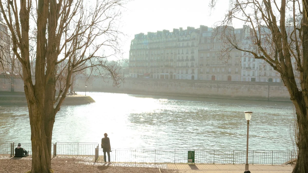 A walker on the Seine quays in the early morning, golden light on the island opposite