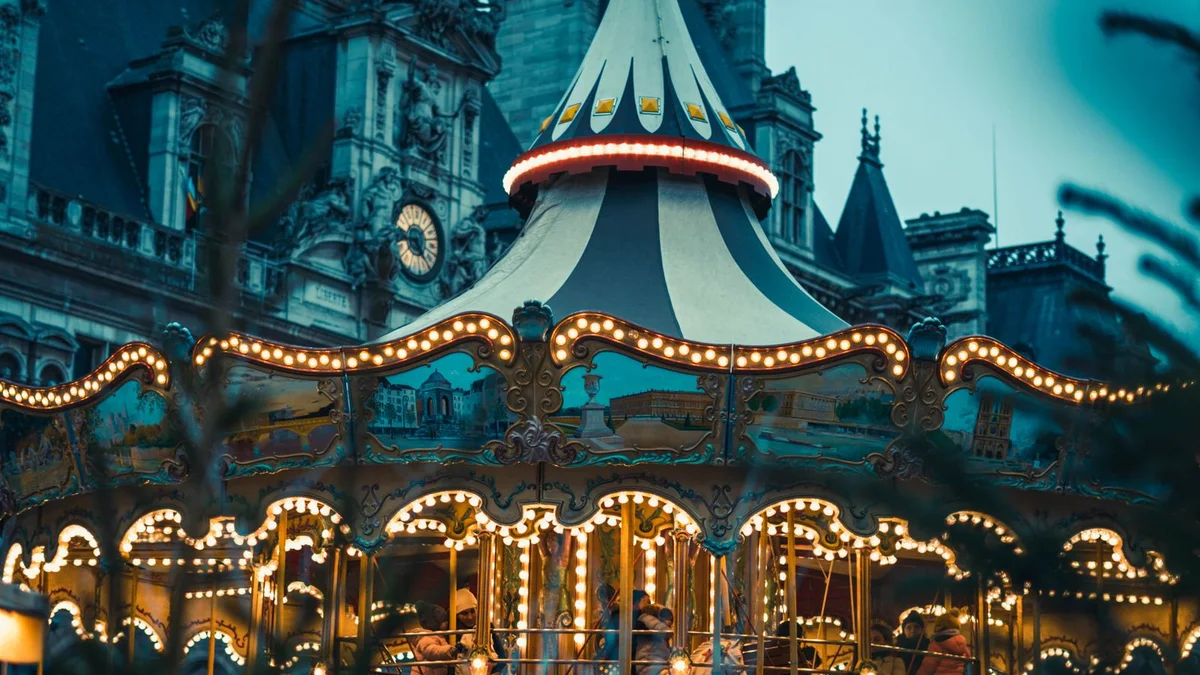 An illuminated carousel at dusk in front of the Paris Hôtel de Ville, in December