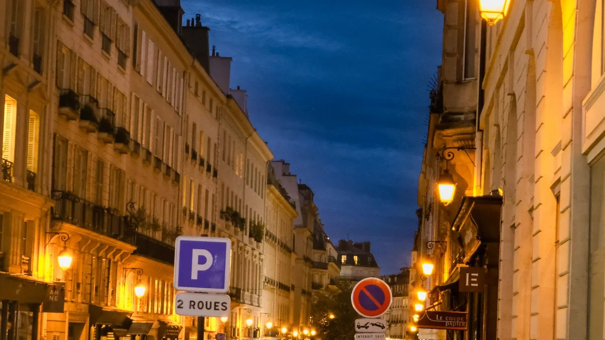 Rue parisienne à la tombée du soir en automne, réverbères allumés sous un ciel bleu nuit