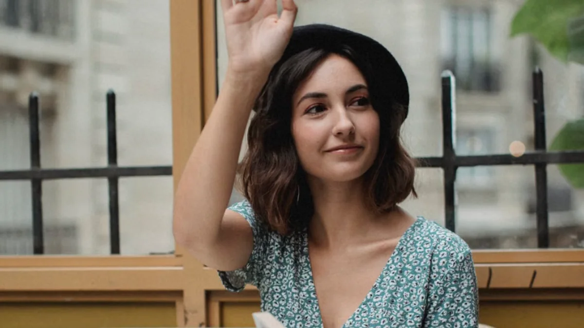 A young woman in a beret waves from a Parisian café terrace, Haussmann buildings in the background