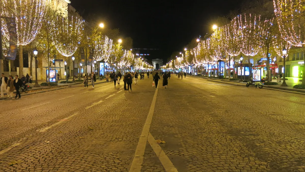 The avenue des Champs-Élysées pedestrianised at night, trees wrapped in white Christmas lights, the Arc de Triomphe at the end